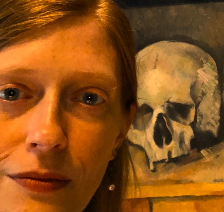 Close-up of the face of Hadley Moore, a white woman, posed next to a painting of a skull.