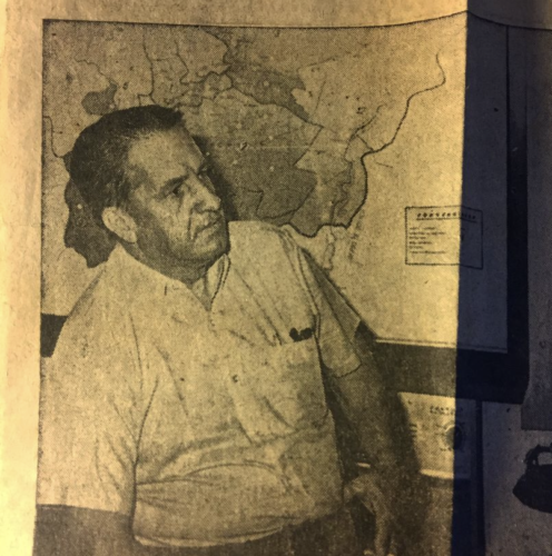 A yellowed newspaper photo of a Colombian man in a short-sleeve button-up shirt in front of a map.