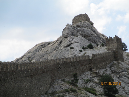 The wall of the fortified city of Sudak beside a pointed stone mountain.