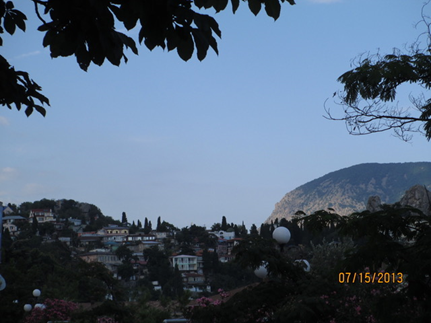 A series of dwellings nestled into trees and mountains against a blue sky.