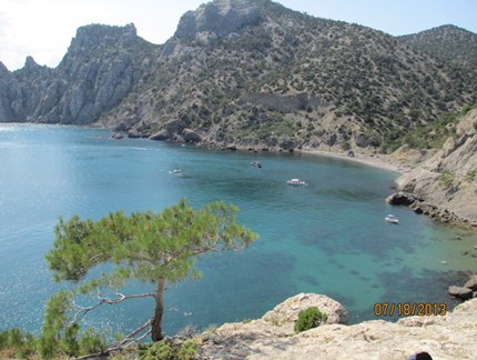 An inlet: bright blue water surrounded by forested mountains and rocky beach.