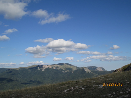 Mountains and a grassy valley against a big blue sky.