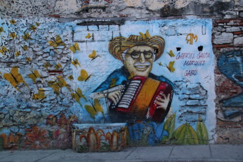 A street mural of Gabriel Garcia Marquez (Gabo) playing an accordion, with butterflies around him