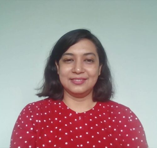 Mandira Pattnaik, an Indian woman wearing a red blouse with polka dots, smiles and stands in front of a soothing blue background