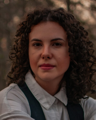 Charis Morgan, a white woman with curly brown hair wearing a white blouse in a natural setting