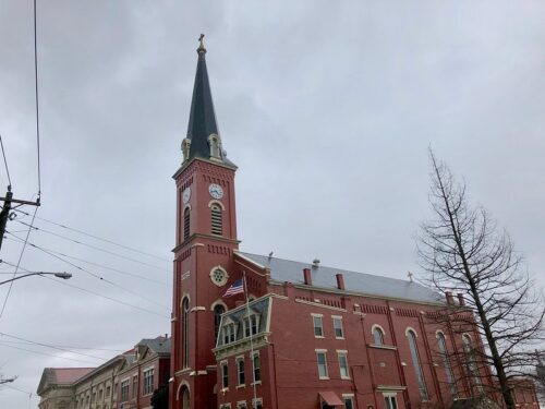 A red-brick church with steeple and side buildings, under a gray sky