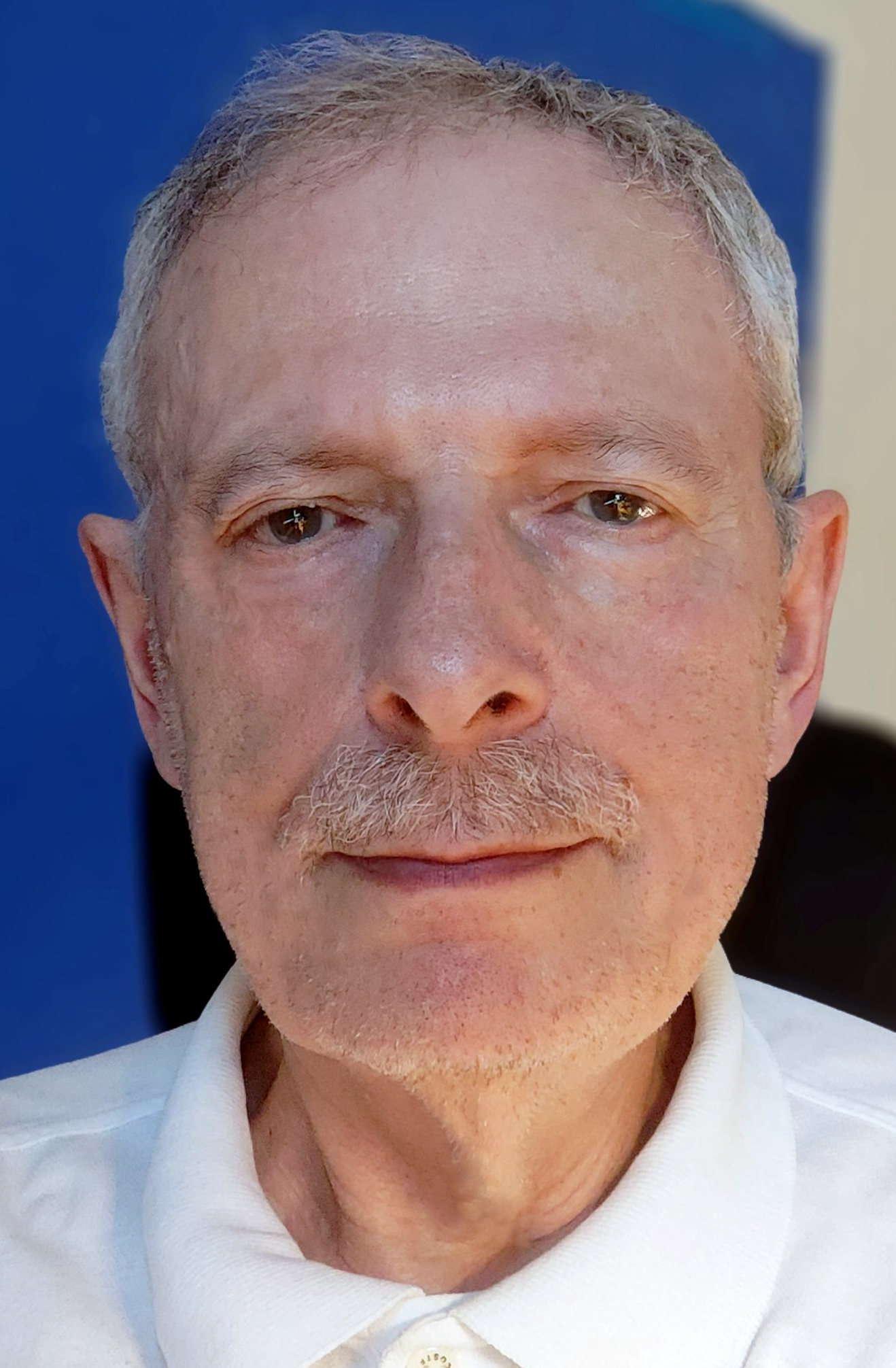 writer Mark Budman, a mustached septuagenarian man facing the camera close-up, wearing a white collared shirt